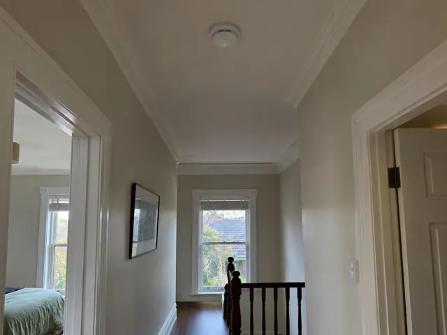 Ceiling-mounted smoke alarm in a hallway with decorative cornices and timber stair balustrade in Naremburn